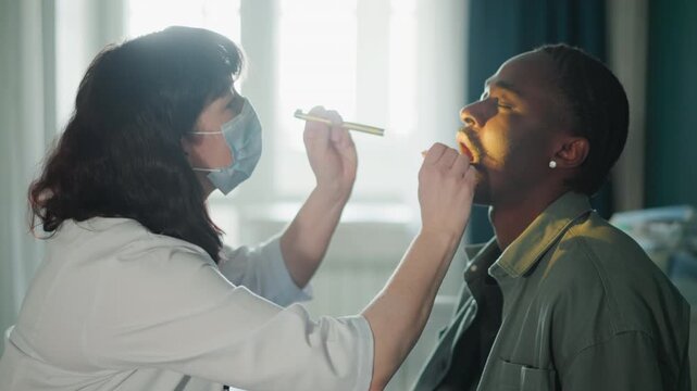 Masked clinician home throat exam with penlight and stethoscope in domestic room methodical inspection of oral cavity and tonsils, PPE and safety protocol visible, daylight through window, calm