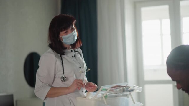 White doctor offering prescription and reassurance to black patient during home consultation, masked professional checks label and explains dosage with steady demeanor and natural window light