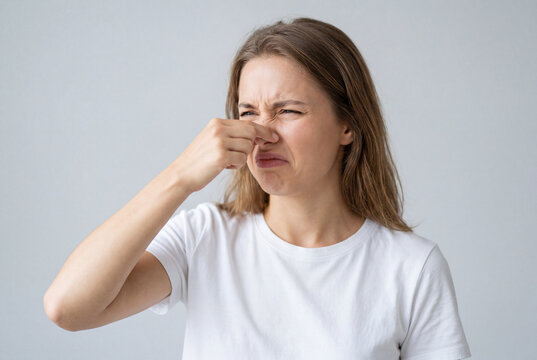 Young woman pinching her nose with her fingers reacting with a natural expression of strong disgust