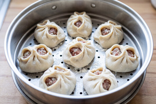 Eight raw meat filled dumplings arranged in a circle inside a stainless steel steamer basket