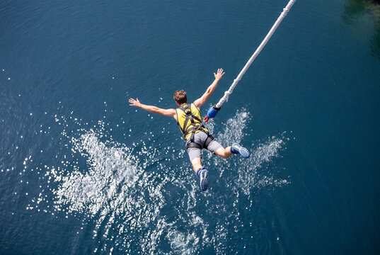Man bungee jumping headfirst with arms outstretched over deep blue water