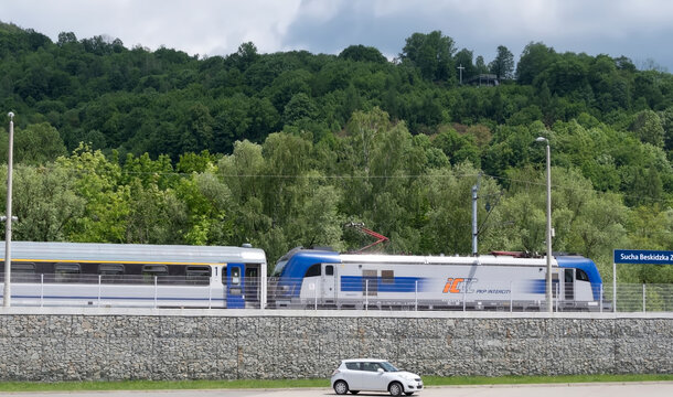 Polska Sucha Beskidzka, 31 maja 2026, 12:46. PKP Intercity &ndash; elektryczny pociąg pasażerski na peronie. Pociąg stoi r&oacute;wnolegle do kamiennego muru, w tle widać bujną zieleń drzew i zalesione zbocze. Nie