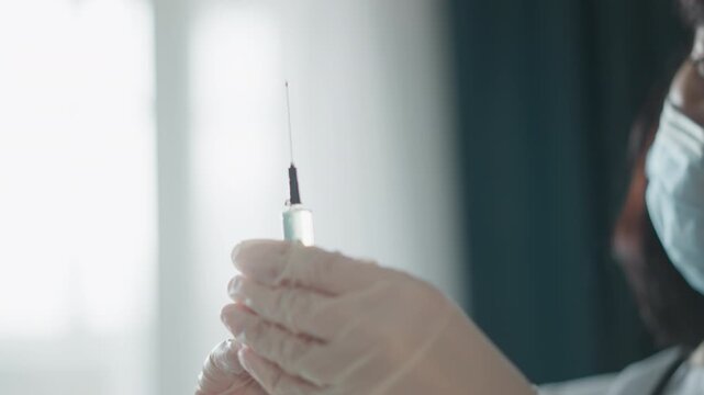 Masked nurse prepares syringe in home, gloved hands drawing clear vaccine from vial, checking for air bubble under soft window light, calm professional setting during home visit, focused sterile