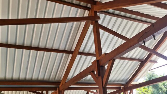Interior view of a gazebo roof structure featuring solid wooden beams and white corrugated metal sheets