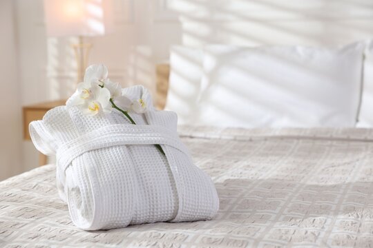 Clean bathrobe with flowers on bed indoors, space for text