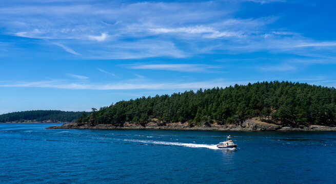 A small cruising powerboat speeds along the rocky, evergreen filled shores of Lopez Island in the San Juan Islands on their boating vacation.