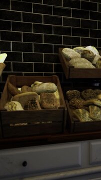 Loaves of bread sit invitingly in wooden crates. Baguettes lean gracefully, their golden crusts glowing against a sleek black tile background. The aroma of freshly baked bread fills the air.