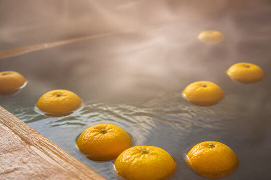 Japanese yuzu citrus bath for the winter solstice, fresh yellow yuzu fruits floating on the steaming hot water of a wooden ofuro tub with soft backlit vapor, a traditional toji seasonal bathing custom