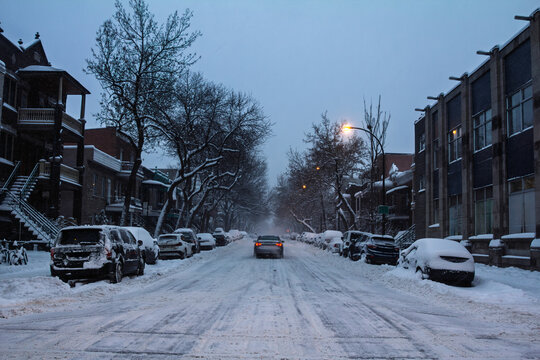 American Residential street in Le Plateau, Montreal, Quebec, Canada, at winter dusk, with parked cars, snow-covered road, duplex houses, streetlights and a quiet neighborhood real estate setting.