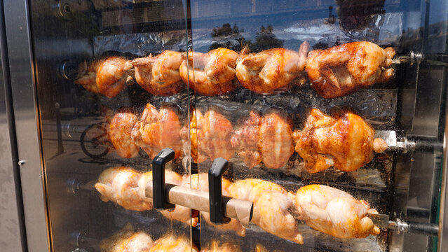 Golden brown chickens cooking slowly on spits inside a rotisserie oven