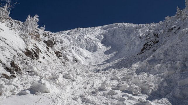 Massive avalanche debris pile covering a steep mountain slope under a clear blue sky