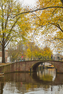 Traveler on historic brick arch bridge over autumn canal in Amsterdam, vertical background with copy space