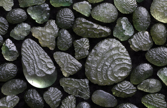 Overhead flat lay of multiple raw moldavite tektite pieces filling frame, varied natural shapes teardrop, disk, irregular splash forms 