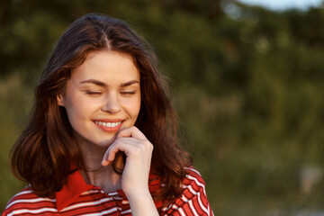 Obraz premium A smiling young woman enjoying nature in a portrait shot. The happy woman reflects a peaceful lifestyle outdoors during a sunny summer day. Concept for wellness, relaxation, and mindfulness.