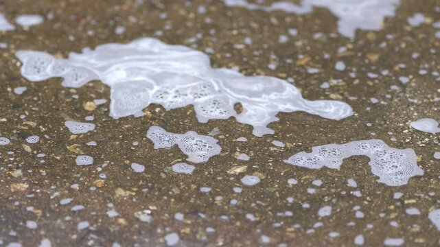 Sea foam beach sand surf water shoreline texture pattern closeup, bubbly tide wash on wet coast, soap foam bubbles on pavement concrete asphalt, outdoor abstract cleaning spill after wash