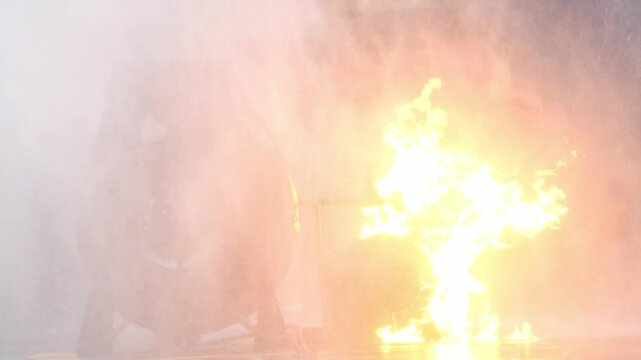 Fire water hose spray on industrial turbine blaze, flame and smoke cooling burning fuel near equipment, firefighter training drill for emergency response, heavy mist safety focus