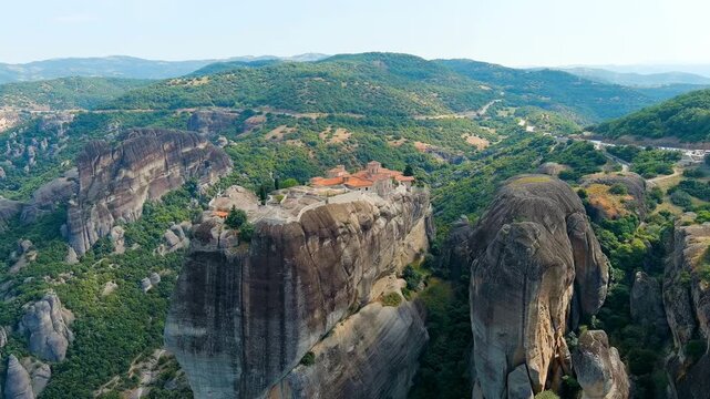 Meteora, Kalabaka, Greece. Monastery of the Holy Trinity, terracotta rooftops and stone walls perched atop a slender sandstone pillar, aerial drone view over the Thessalian valley. Drone footage