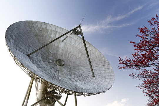 A large satellite dish antenna operates under the clear blue sky.