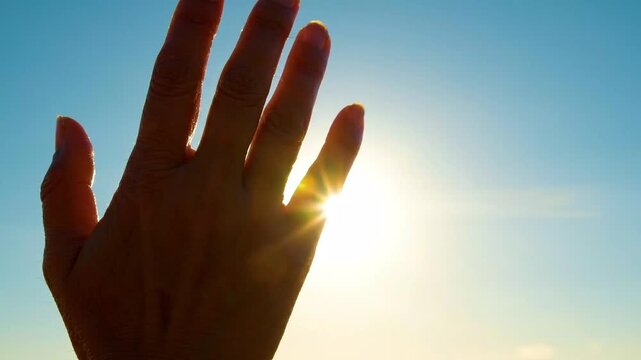 Hand Silhouette Reaching for the Bright Sun in a Clear Blue Sky
