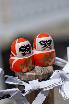 Two Daruma Dolls Tied to Wooden Post with White Paper Streamers