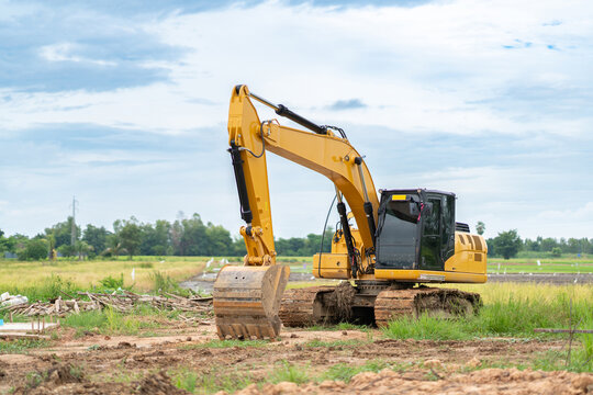 Yellow tracked excavator standing on an open ground earthwork site against a cloudy sky background.