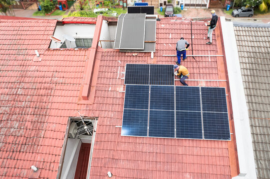 Aerial view of workers installing solar photovoltaic or PV panels onto red rooftop of residential house in Malaysia