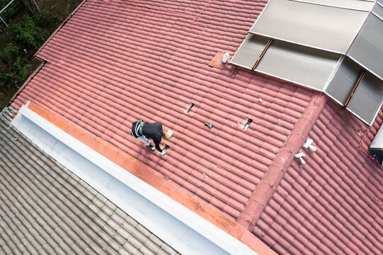 Aerial view of worker installing metal brackets onto house roof truss to prepare for solar photovoltaic or PV panels installation onto red rooftop of residential house in Malaysia