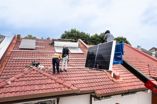 Aerial view of workers transporting solar photovoltaic or PV panels with crane onto red rooftop of residential house to install in Malaysia