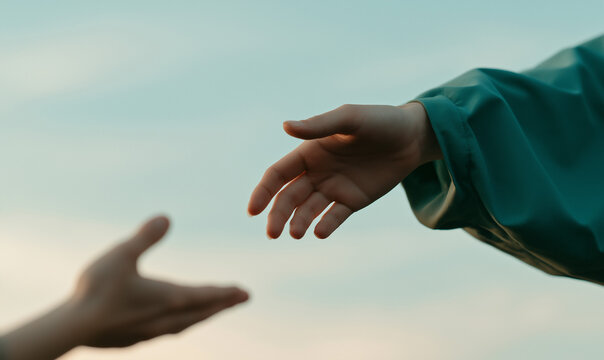 a close up shot of a hand in the foreground reaching up towards a hand extending down from the upper left.