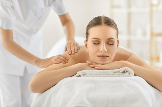 Relaxed woman enjoying massage from professional masseur, lying on couch and keeping eyes closed, posing in spa salon, helping to reduce pain or muscle tension. Wellness and health care