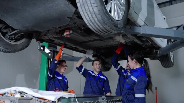 A team of automotive technicians celebrates a successful electric vehicle repair while working around a vehicle lift and battery service equipment in a workshop.

