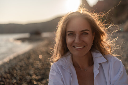 Woman beach sunset. Smiling young woman enjoying golden hour on a pebble beach, radiating natural beauty and happiness