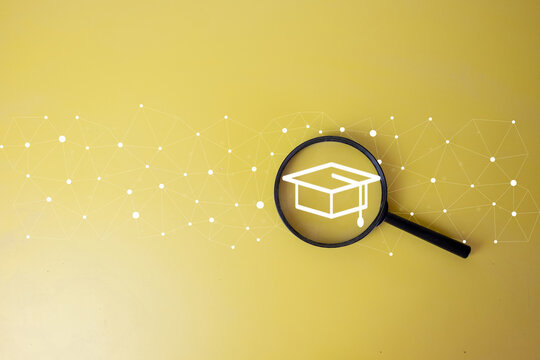Online education and scholarship search concept. Magnifying glass focusing on a digital graduation cap graphic with network lines on a yellow background with ample copy space.
