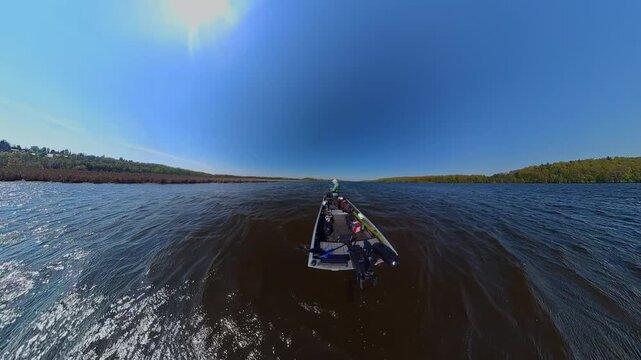 Fisherman is fishing on lake from boat casting spinning rod at daylight. Angler is standing in an equipped boat and catching fish while trolling. Man holds spinning rod while offshore during sunny day