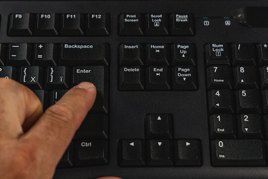 Hand pressing enter key on computer keyboard at office desk during work