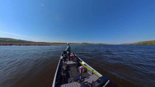 Fisherman is fishing on lake from boat casting spinning rod at daylight. Angler is standing in an equipped boat and catching fish while trolling. Man holds spinning rod while offshore during sunny day