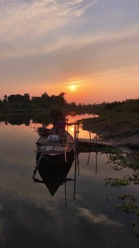 A local farmer working by a serene river during sunset loading hay onto a traditional wooden boat