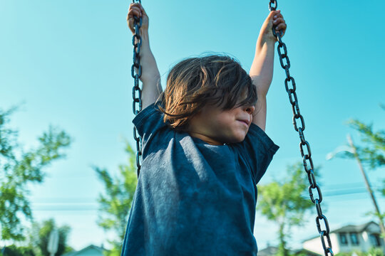 Boy holding swing chains with arms raised seen from below