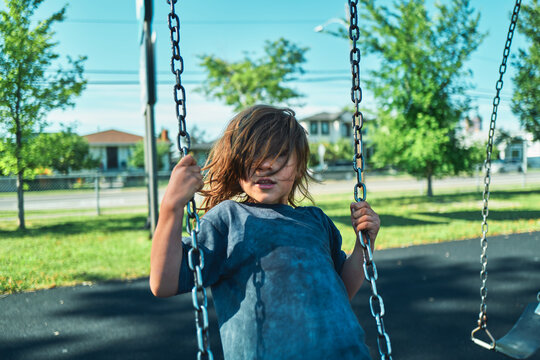Boy sitting on a playground swing with windswept hair