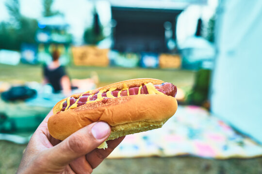 Hand holding a hot dog with mustard and ketchup at an outdoor concert