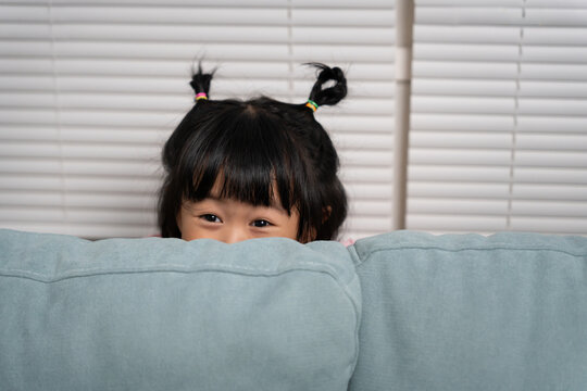 little asian children kid playing hide and seek standing behind the sofa, Adorable child having fun in the home. happy family have fun with kids, activity, learning, activity, game, meditation