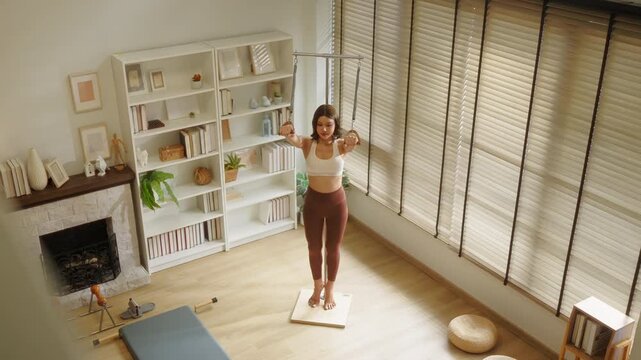 An overhead view captures a pilates instructor guiding her client through a standing suspension ring exercise, both engaged in focused training a dynamic top-down shot of aerial pilates coaching.