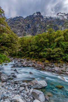 Gebirgsbach bei Christie Falls mit Blick auf zerklueftete Gipfel der Darran Mountains, Kiesbett und Felsbrocken im Vordergrund, Fiordland National Park, Southland, Suedinsel, Neuseeland