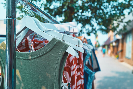 Shirts on white hangers on a sidewalk clothing rack outside a shop