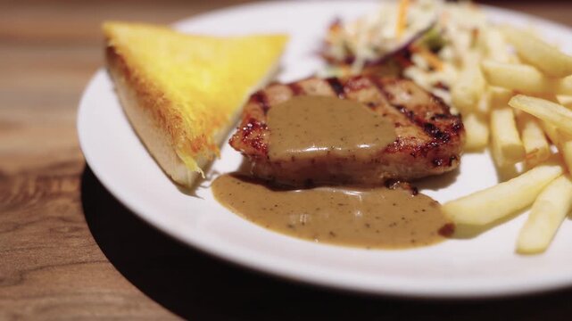 Grilled pork steak topped with creamy black pepper gravy, served with golden french fries, buttered toast, and fresh coleslaw salad on a white plate. Delicious restaurant dinner meal concept.