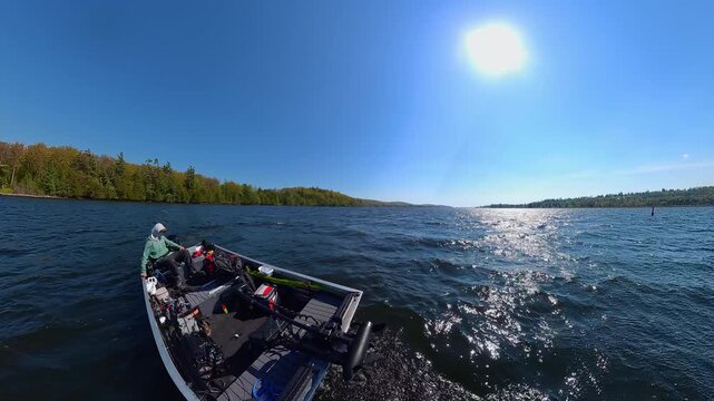 Small power boat speeding along the surface of the North American lake. Fishing boat with outboard motor floats on the water waves in the lake creating wake and white foamy trace.