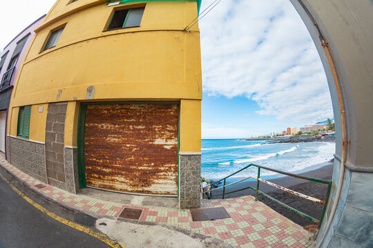 Fisheye view of Tenerife coast and old yellow building with rusty garage door and copy space
