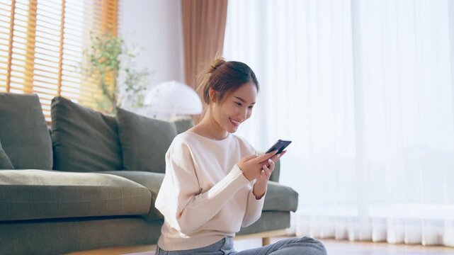 Happy young asian woman relax on comfortable couch at home texting messaging on smartphone, smiling girl use cellphone, chatting online message, shopping online from home