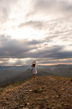 Mountain summit exploration featuring a woman in a white dress standing on a rocky hill during a golden hour sunset