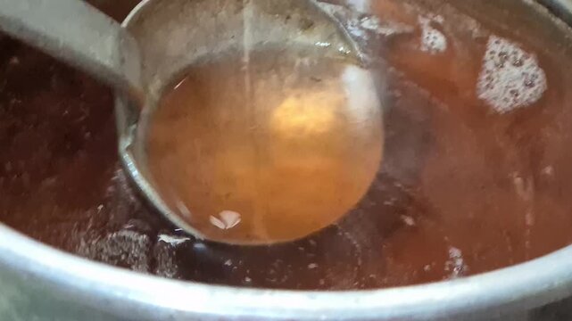 Close up of stirring hot brown broth soup with a metal ladle in a stainless steel pot